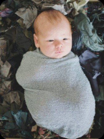 A calm newborn swaddled in a soft sage wrap